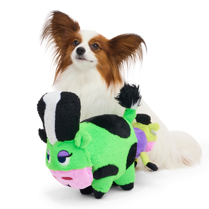 Papillonhond zit achter de groene koeknuffel met de kleine koe aan de staart