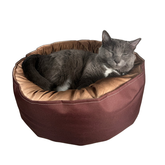 Grijze kat slaapt in rond kattenbed met bruine rand en beige kussen