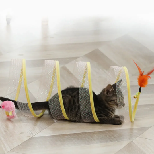 Grijs gestreepte kat ligt in de gele spiraaltunnel met roze speelmuisje