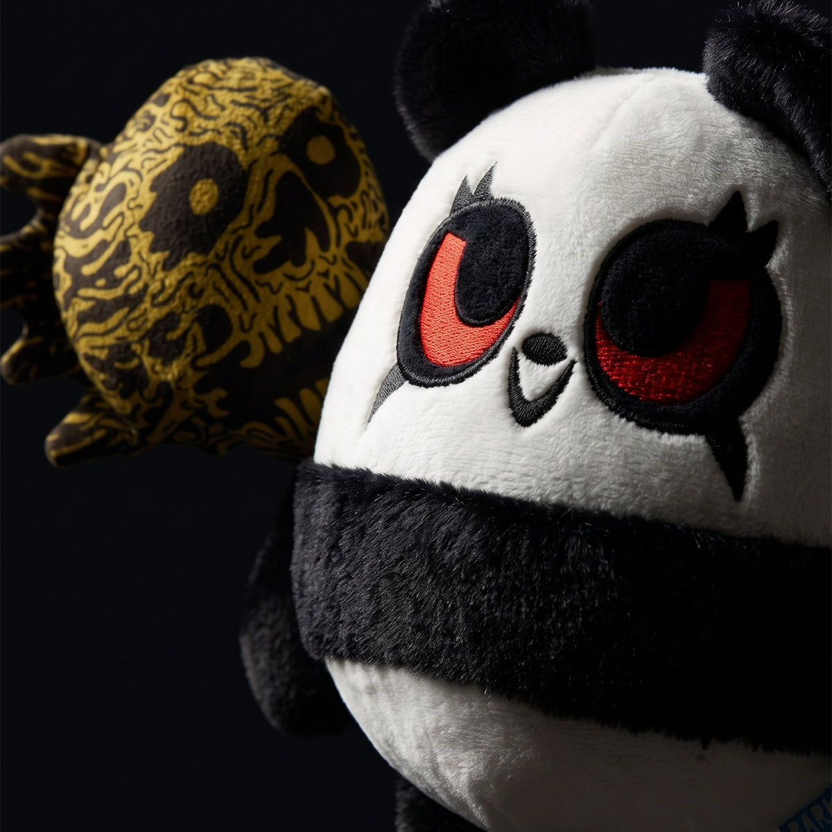 De pandaknuffel naast een goud-zwart bedrukt speeltje tegen donkere achtergrond
