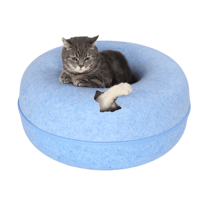 Grijze kat ligt in de kattengrot, witte poot steekt door kattenkopgat