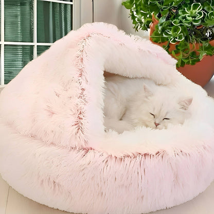 Witte langharige kat slaapt in roze kattenmand naast een plant bij het raam