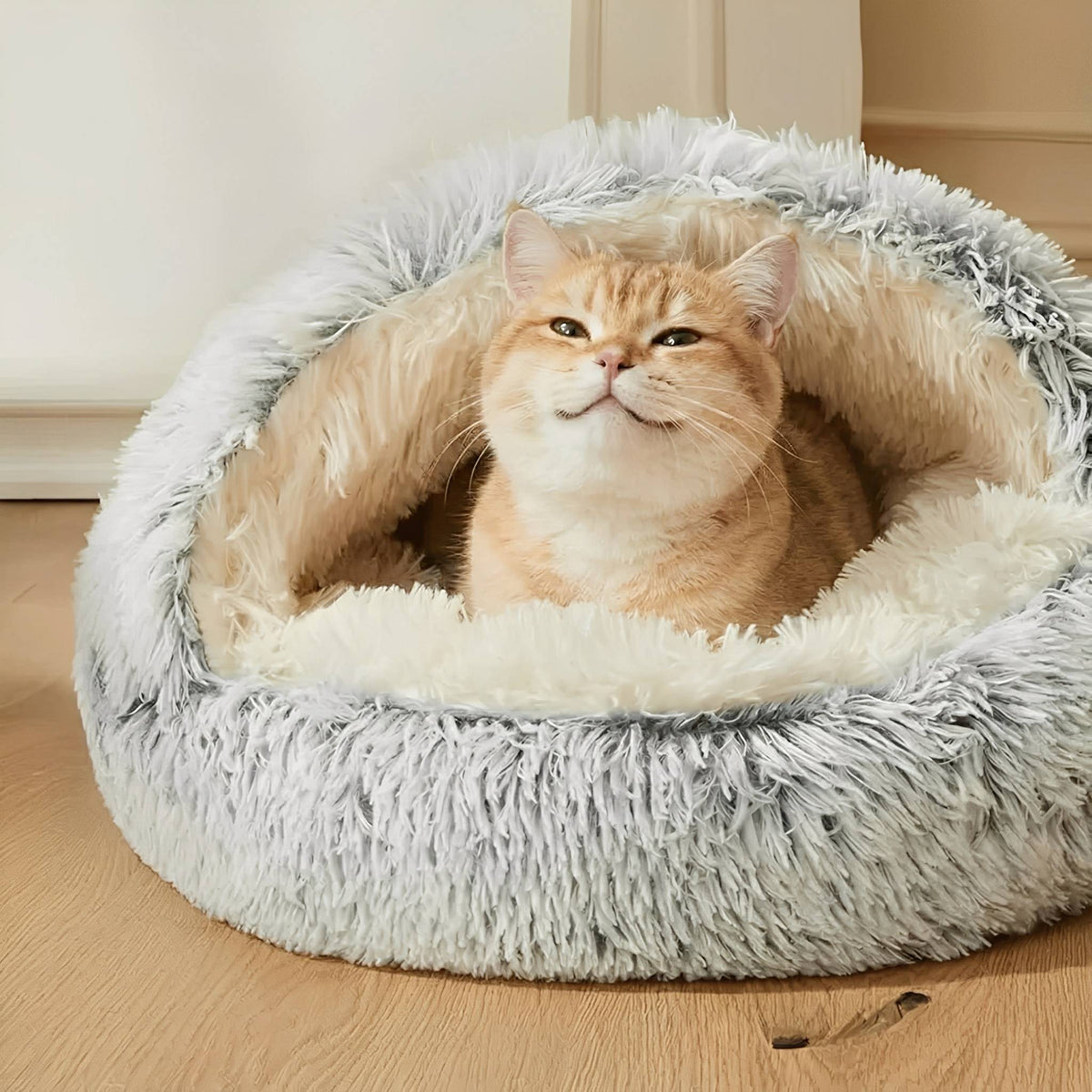 Grijze pluche kattenmand in grotvorm met rode kat die tevreden in de opening zit