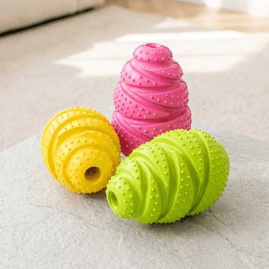 Drie rubberen snackdispensers voor honden in geel, roze en groen op een grijs kleed