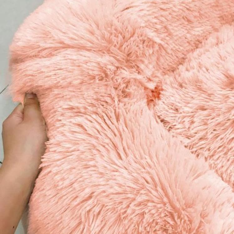 Hand knijpt in de lange roze pluche stof van de kattenmand