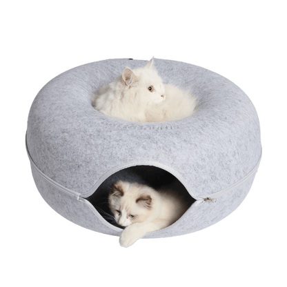 Twee witte katten in een lichtgrijze kattengrot, één bovenop en één in de opening