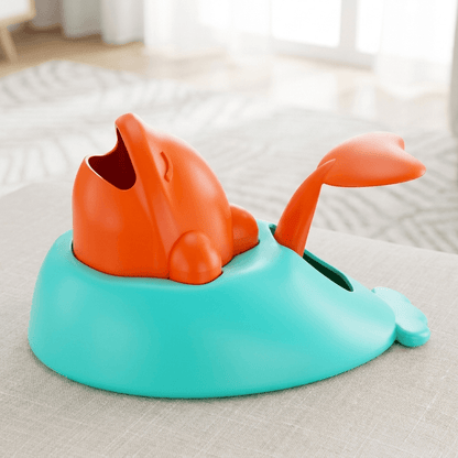 Snackdispenser in walvisvorm met oranje walvis op turquoise voet, op een grijze bank